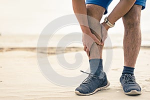 Man runner hold his sports injured leg on the beach background