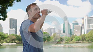 Man runner jogging in park. Fit male sport fitness running training. Drinking water from bottle