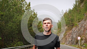 Man running alone in forest at daytime. Male athlete practicing morning jog workout. Muscular young man running on mountain road.