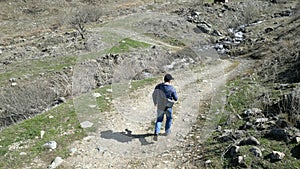 A man running along a road towards a river. Mountainous terrain, trees, rocks