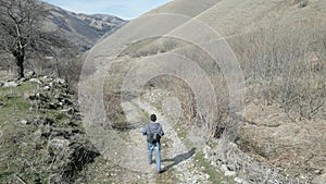 Man is running down mountain road. High mountains, trees, old houses, rocks, sky