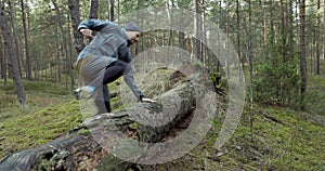 Man running on forest trail and jump over old fallen tree. slow motion