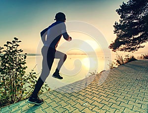 Man running on lake shore pavement during sunrise or sunset