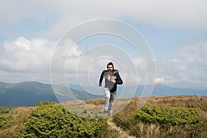 Man runs on green meadow in mountain on cloudy sky