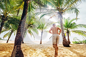 Man runs under palm trees towards the ocean sand beach