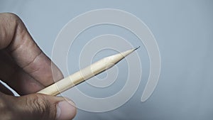 A man's Asian hand is sharpening a wooden pencil, rotating it until the tip becomes pointed on an isolated white background.