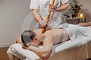 Man`s back during traditional thai massage with stick. Oriental alternative medicine with wooden tools. Body care and SPA in