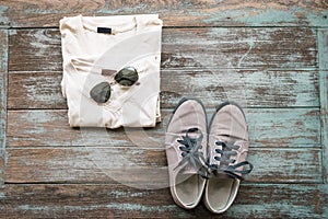Man's clothing, sunglasses, and shoes lay on wood vintage background,