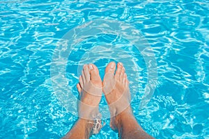 Man`s feet against blue water of swimming pool