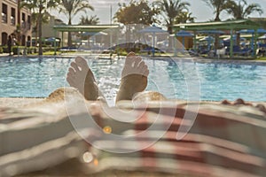 Man's feet on the background of a swimming pool. man relaxing by the pool, men's feet on the pool background. toned