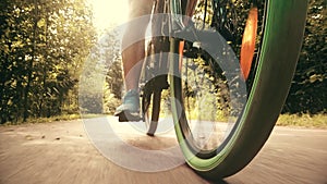 Man`s feet on pedals and moving bicycle in a summer park, low angle view