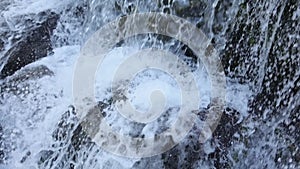 Man's feet standing on the rock with white water gushing over the weir with a building above