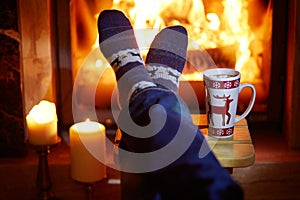 Man`s feet in warm socks with large mug of hot chocolate and murshmallows near fireplace