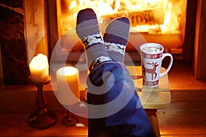 Man`s feet in warm socks with large mug of hot chocolate and murshmallows near fireplace