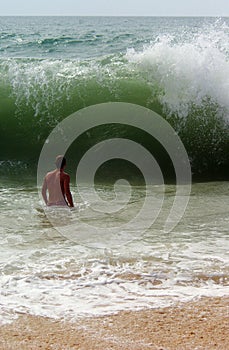 A man's figure in front of a big wave breaking on a beach