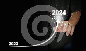 A man`s finger draws an upwards curved line from 2023 to 2024. New Year, Christmas, start-up, new business, setting a personal