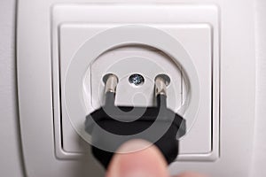 A man`s  finger plugging a plug into a wall socket