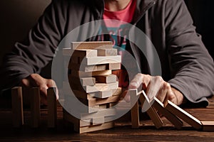 Man's fingers prevent the wooden block game stick from falling domino