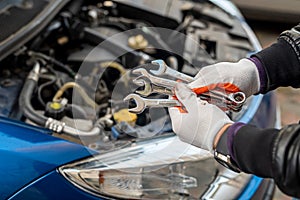 Man& x27;s gloved mechanic& x27;s hand holds car tools near a painted car with an open hood