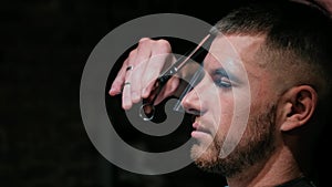 Man's hair cutting by barbers scissors and comb with barbershop logo behind in slow motion. Mans hands making male