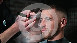 Man's hair cutting by barbers scissors and comb with barbershop logo behind in slow motion. Mans hands making male