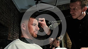 Man`s hair cutting by barbers scissors and comb with barbershop logo behind in slow motion. Mans hands making male