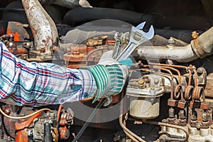 Man's hand with adjustable wrench near old diesel engine