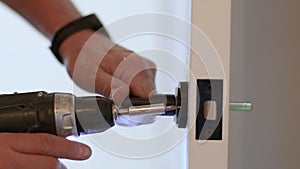 A man& x27;s hand attaches to the door handle with screws and a screwdriver, close-up