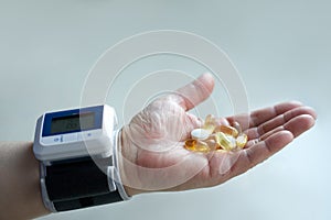 A man`s hand with a blood pressure monitor on his wrist and pills in the palm of his hand. Selective focus