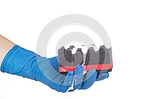 A man`s hand in a blue household glove holds a corrugated black sponge, dishwashing detergent is applied. On white background.