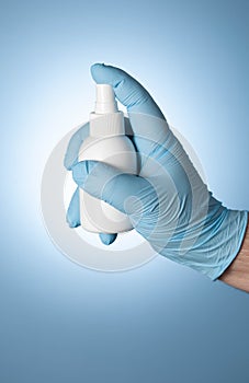 A man`s hand in a blue medical glove holds a white plastic spray from covid-19