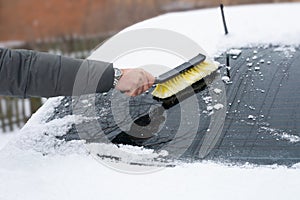 A man's hand with a brush cleaning the rear window of a car from snow in the winter season