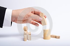 The man`s hand of a businessman in a business suit holds a wooden figure of a man in his hand and moves another figure