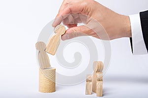 The man`s hand of a businessman in a business suit holds a wooden figure of a man in his hand and moves another figure