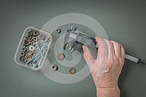 A man\'s hand with a caliper and fastening material on a gray background