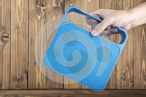 Man's Hand Carrying Blue Handy Speaker on Wooden Background