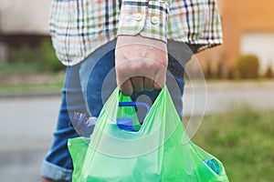 Man`s hand carrying green plastic bag full of plastic bottles ready for recycling, copy space