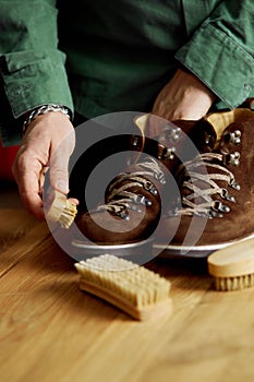 Man`s hand clean suede shoes, boots with a brush on wooden background