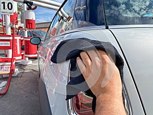 Man`s hand cleaning the car with black microfiber cloth. Hand wipe down surface of car