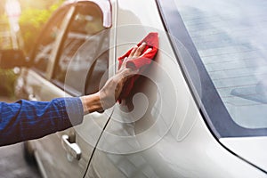 Man`s hand cleaning car & drying vehicle with microfiber cloth. Hand wipe down paint surface of shiny blue sedan after polishing