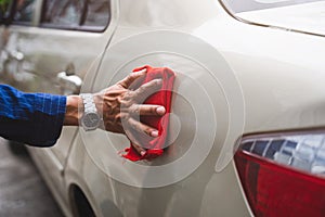 Man`s hand cleaning car & drying vehicle with microfiber cloth. Hand wipe down paint surface of shiny blue sedan after polishing