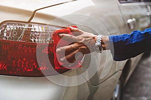 Man`s hand cleaning car & drying vehicle with microfiber cloth. Hand wipe down paint surface of shiny blue sedan after polishing