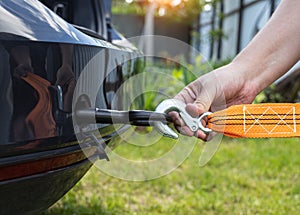 A man`s hand clings a tow rope to a tow hook in a passenger car, close-up. Summer