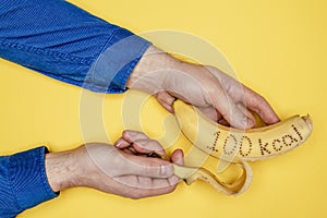 Man`s hand in a corduroy shirt holds a banana on the peel of which is written