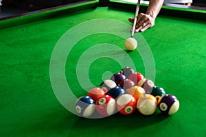 Man`s hand and Cue arm playing snooker game or preparing aiming to shoot pool balls on a green billiard table