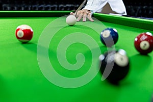 Man`s hand and Cue arm playing snooker game or preparing aiming to shoot pool balls on a green billiard table