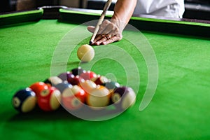 Man`s hand and Cue arm playing snooker game or preparing aiming to shoot pool balls on a green billiard table. Colorful snooker