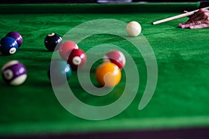 Man`s hand and Cue arm playing snooker game or preparing aiming to shoot pool balls on a green billiard table. Colorful snooker