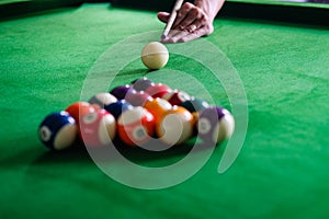 Man`s hand and Cue arm playing snooker game or preparing aiming to shoot pool balls on a green billiard table. Colorful snooker