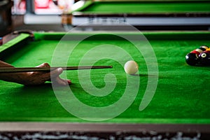 Man's hand and Cue arm playing snooker game or preparing aiming to shoot pool balls on a green billiard table. Colorful snooker